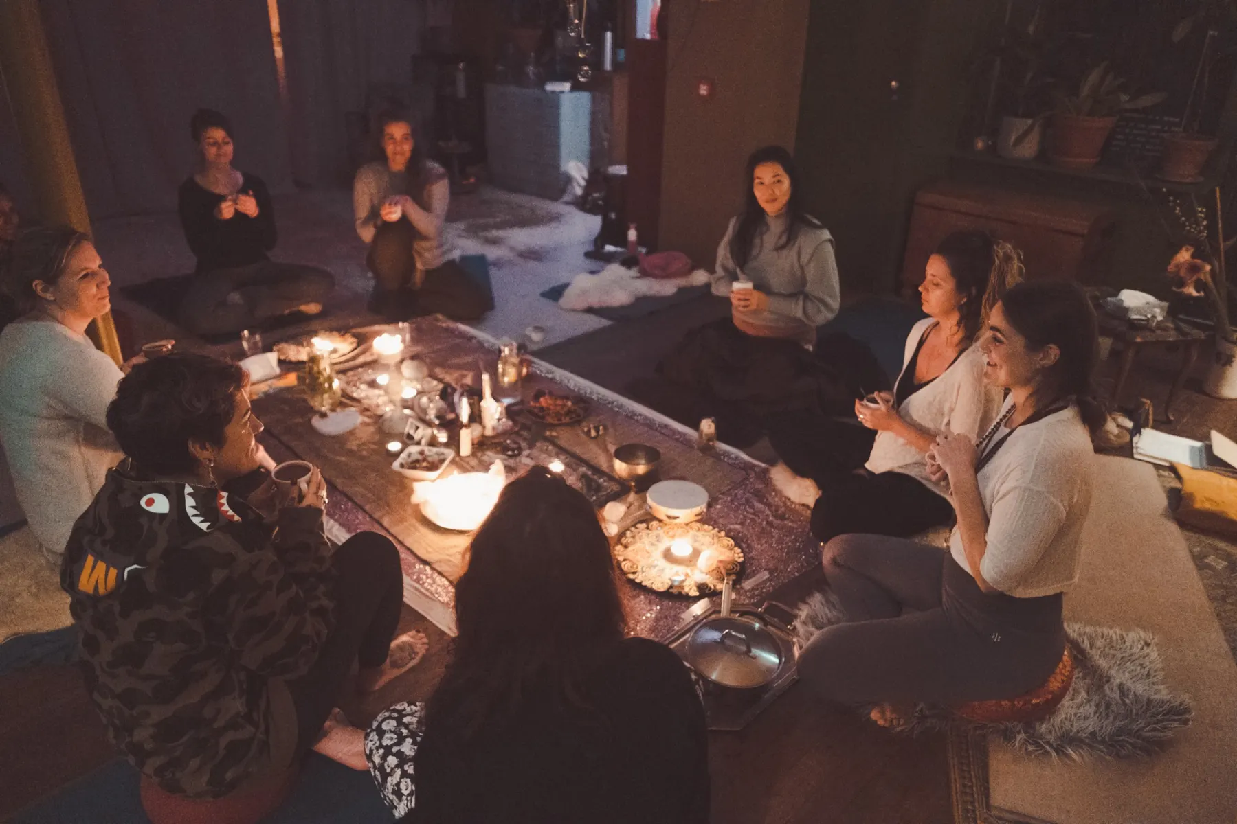 Women in a circle around a candlelit table in a warmly lit room