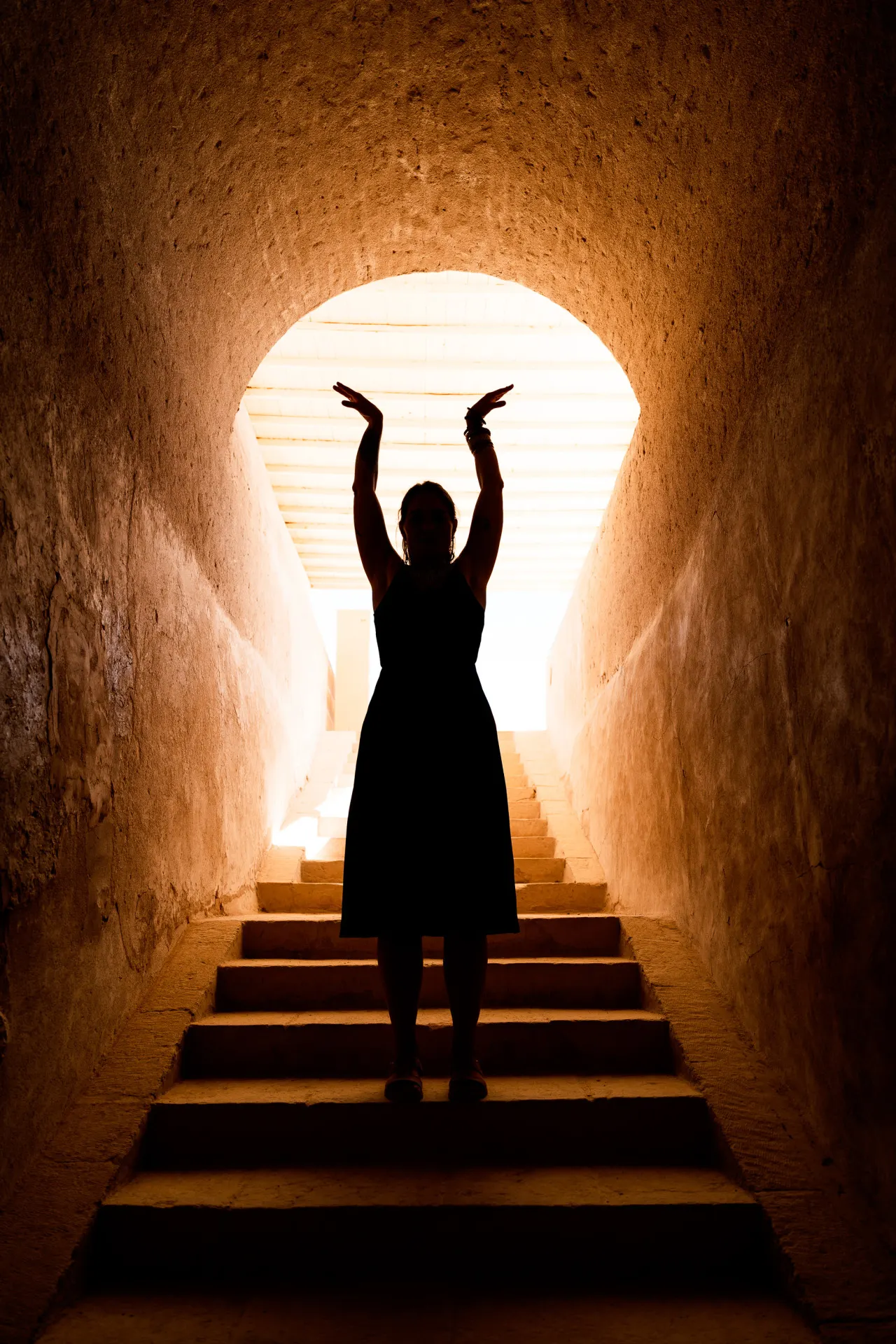 Silhouet met geheven armen in een zonovergoten tempelgang in Egypte