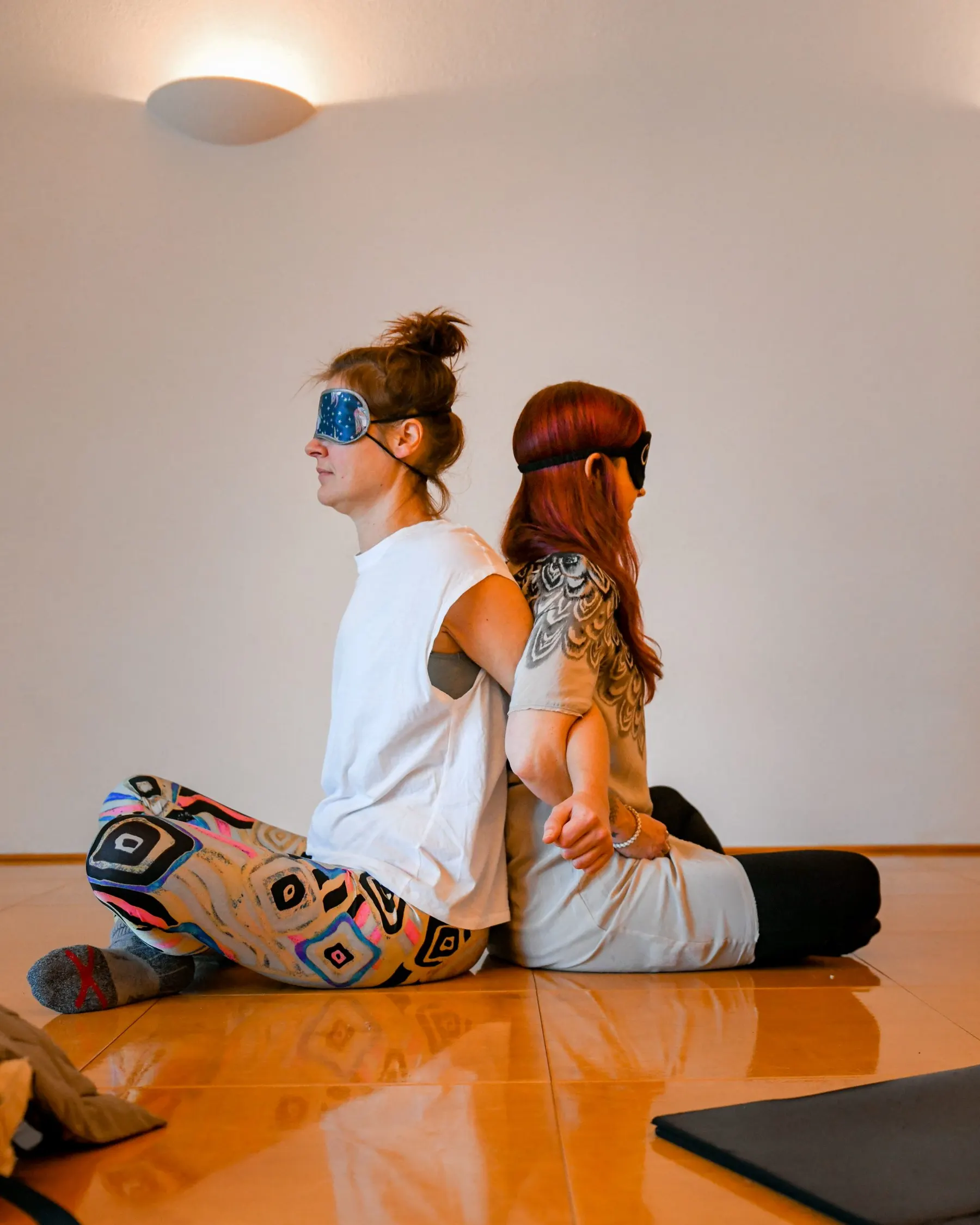 Twee vrouwen met oogmaskers zitten rug aan rug op de vloer