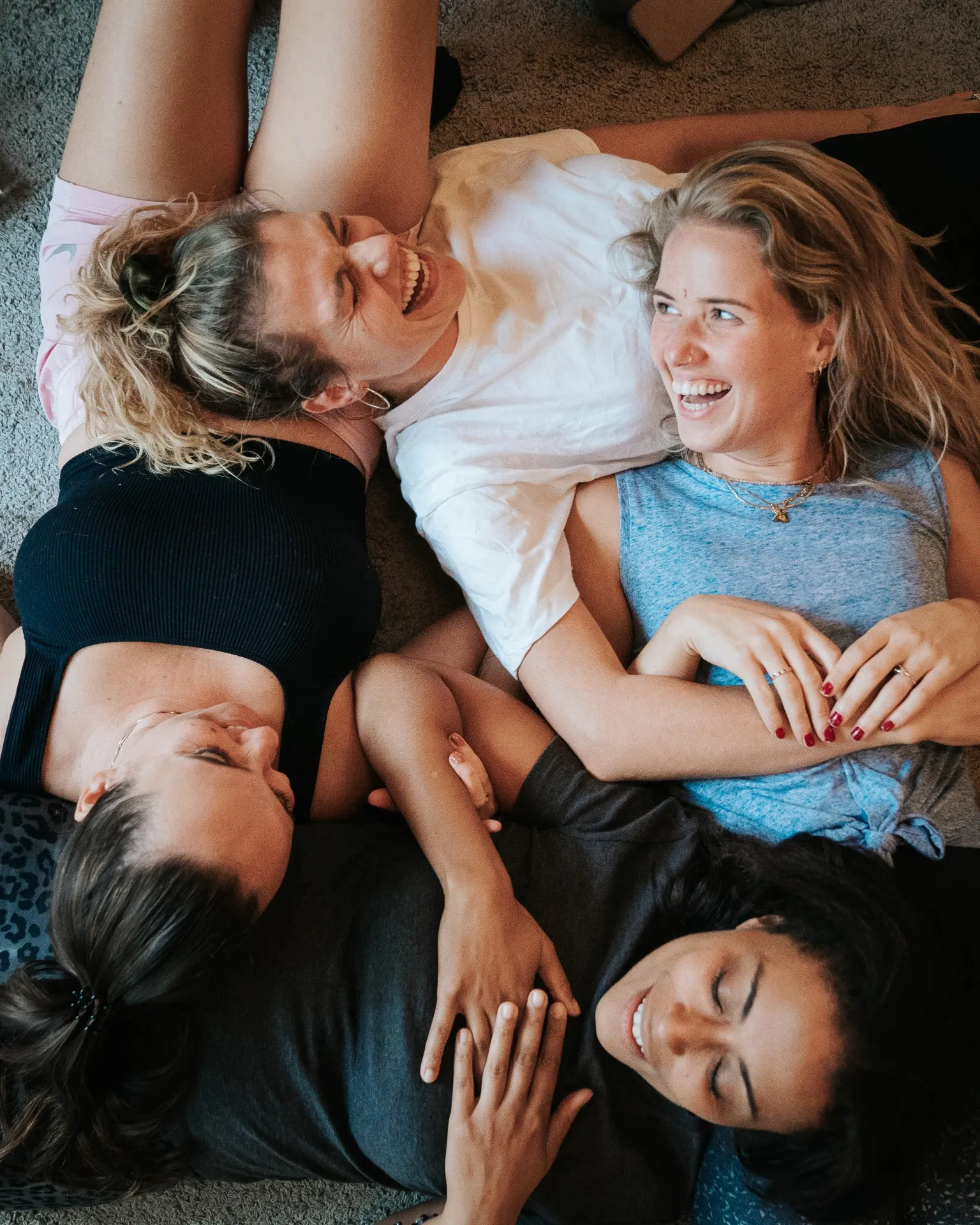 Vrouwen liggen lachend op de vloer, de hoofden bij elkaar
