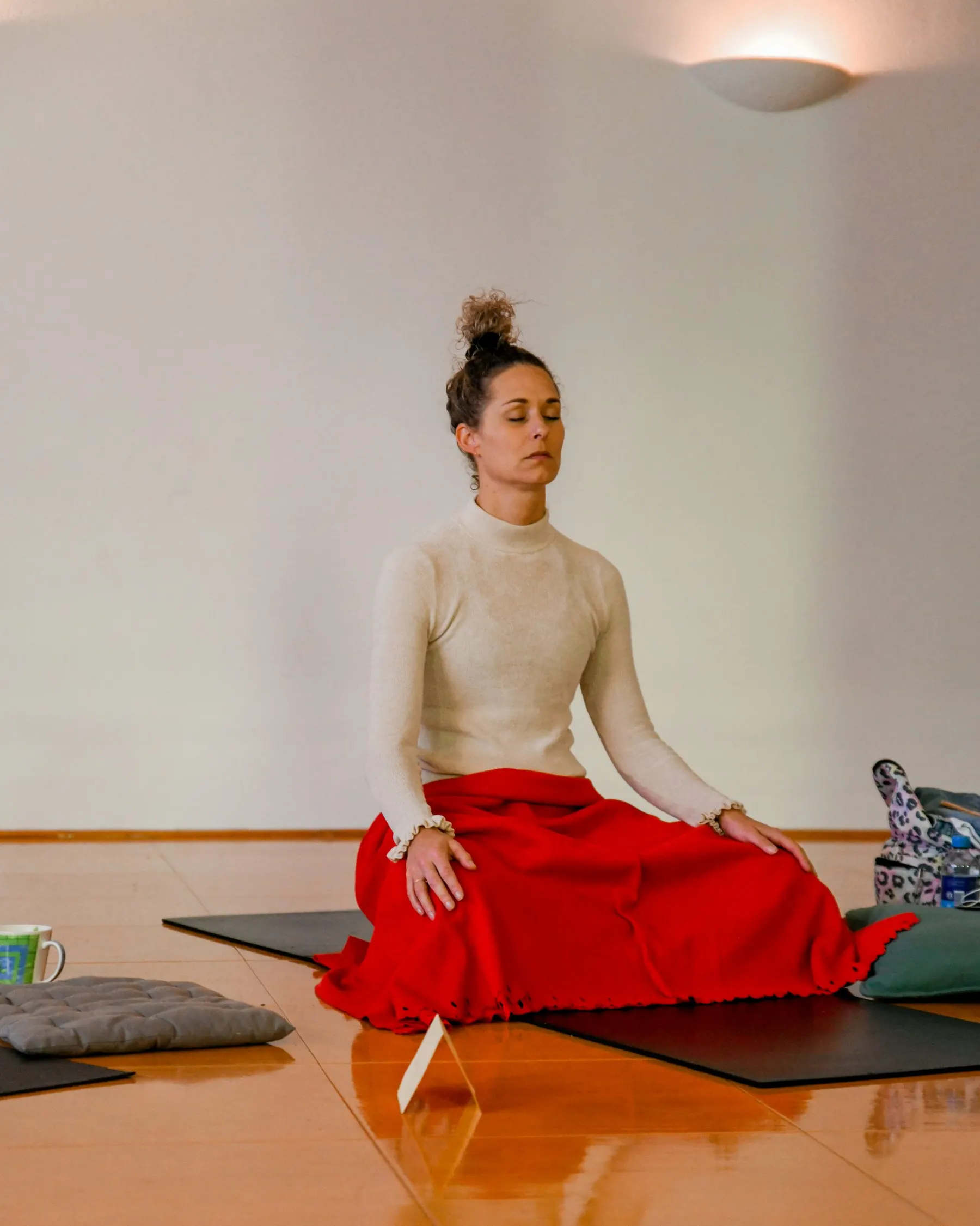 A woman in a red skirt meditating alone in a bright room